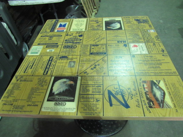 Laminate Table Top With A Square Edge And Assorted Advertisements On A Pedestal Base. 32X32X30
