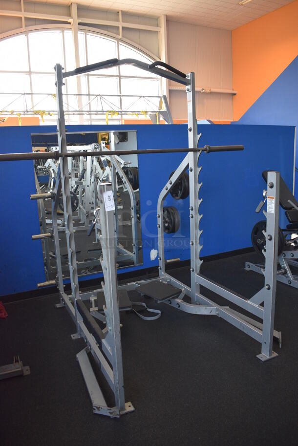 NICE! Hammer Strength Gray Metal Floor Style Squat Rack w/ Olympic Bar. Does Not Include Weight Plates. BUYER MUST REMOVE - Unit May Need Disassembly For Removal. 65x73x91. (weight room)