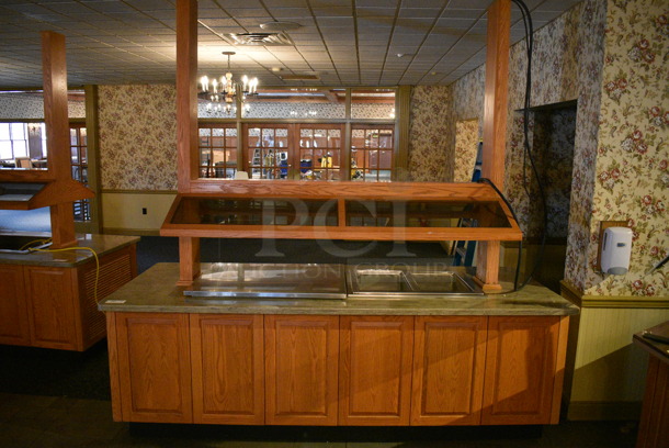 Portable Buffet Station w/ Flat Top and 2 Well Steam Table, Sneeze Guard and Wooden Exterior on Commercial Casters. BUYER MUST REMOVE. 102x42x101. Unit Was In Working Condition When Restaurant Closed. BUYER MUST REMOVE. (buffet)