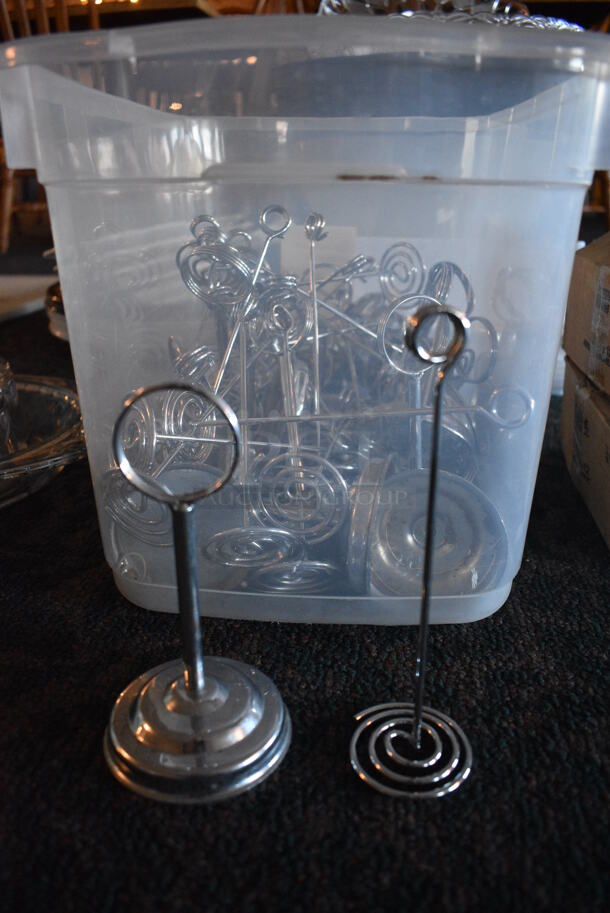 ALL ONE MONEY! Lot of Various Metal Countertop Table Number Holders in Clear Bin! Includes 2x2x7. 16.5x11x11. (main dining room) - Image 1 of 3