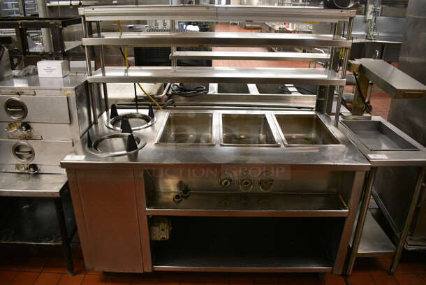 Stainless Steel Commercial Electric Powered 3 Bay Steam Table w/ 2 Plate Return Chutes, Double Over Shelf, 2 Warming Strips and Under Shelf on Commercial Casters. 63x44x64.5. Unit Was In Working Condition When Restaurant Closed. (kitchen)