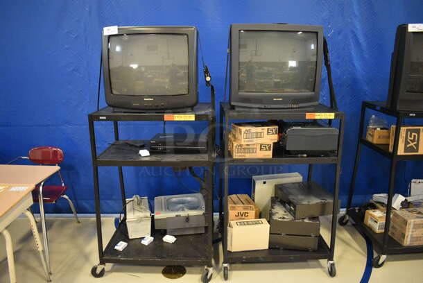 2 Black Metal AV Carts w/ Contents Including Sharp TV, GoldStar TV, VHS Player, Projector. 32.5x27.5x48. 2 Times Your Bid! (Middle School Gym)