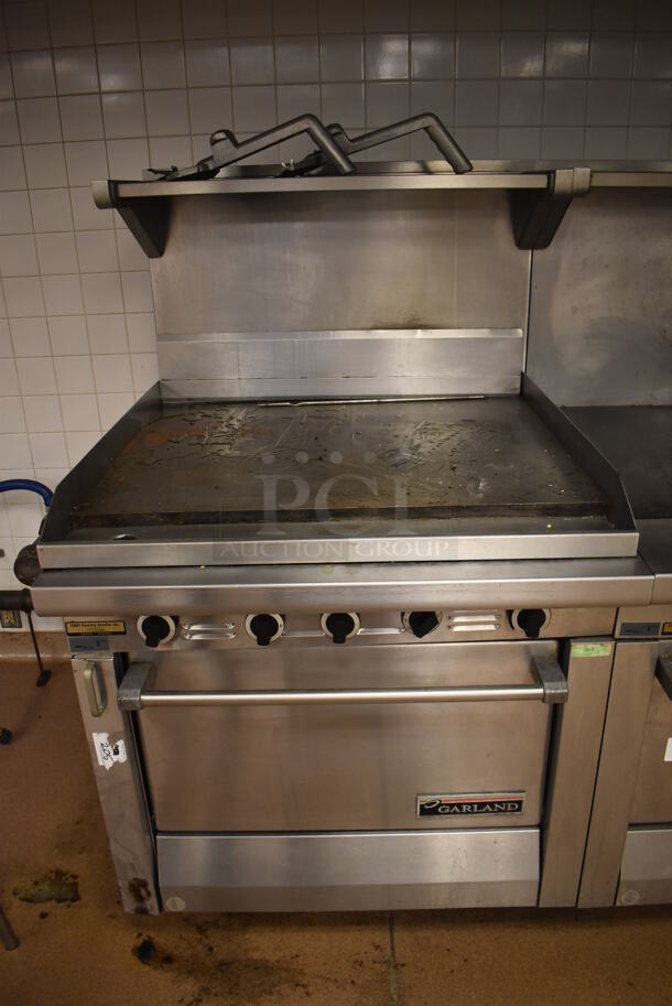 Garland M47R Stainless Steel Commercial Floor Style Natural Gas Powered Flat Top w/ Oven, Over Shelf and Back Splash. BUYER MUST REMOVE. 34x38x58. (Education Kitchen 2) - Image 1 of 7
