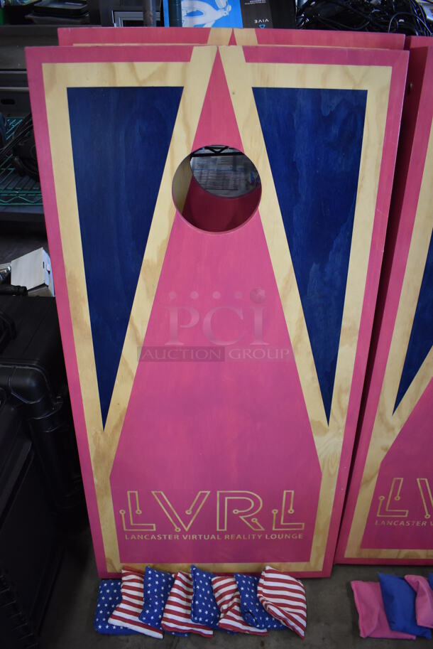 2 Wooden Pink and Blue LVRL Corn Hole Boards w/ 2 Blue Wooden Burky Boards, 4 Blue Starred Bean Bags and 4 Red and White Striped Bean Bags. 24x48x4, 23x23x39, 23x23x63. 2 Times Your Bid!