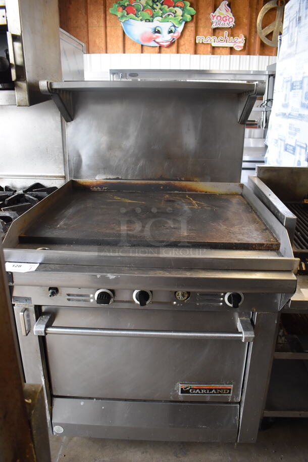 Garland Natural Gas Powered Commercial Stainless Steel Oven With Steel Racks And Top Griddle With Overshelf On Galvanized Legs.  - Image 1 of 7