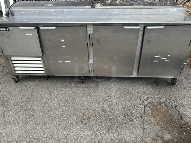 One Leader 4 Door Refrigerated Prep Table With 3 Racks On Casters. Model# PT-96SC. 115 Volt. 96X34.5X43. - Image 1 of 2