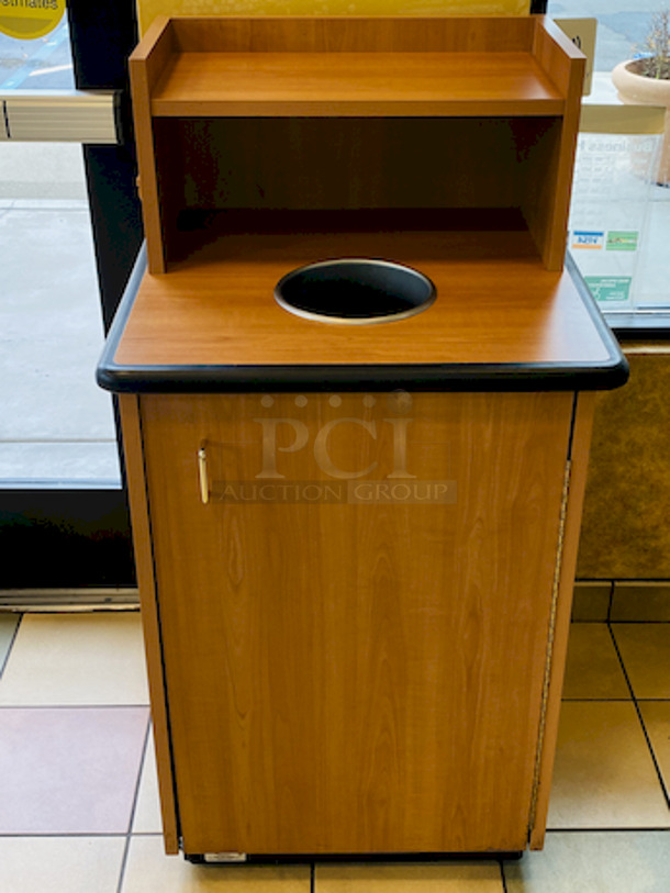 BEAUTIFUL! Plymold Round Drop Top Waste Receptacle with Tray Shelf, With 35 Gallon Liner. 
26x26x48

High pressure commercial laminate top and cabinet
Molded polyurethane edge designed for high traffic areas
8" Drop hole with Dur-A-Edge finish
Provides hygienic seal between laminate and receptacle edge
1.5" Radius corners on top
Rolled edge profile
1-1/8" thick 45 lb density particleboard core
Underside has phenolic backer to protect from moisture
Includes 35 gallon liner with casters
Tray shelf is 21.5"W x 11.25"D
Satin Nickel hinge and door pull
Leveling glides included - Image 1 of 4
