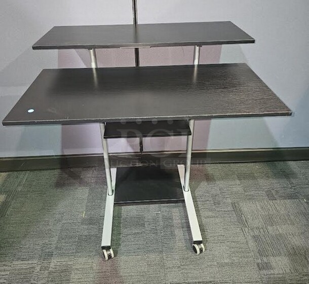 Adjustable-height mobile workstation with silver metal framing and black wooden surfaces. This workstation is on wheels and can be easily moved. In great used condition! Measures 44” H x 39.5” W x 33” D.  

 - Image 1 of 3