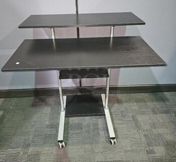 Adjustable-height mobile workstation with silver metal framing and black wooden surfaces. This workstation is on wheels and can be easily moved. In great used condition! Measures 44” H x 39.5” W x 33” D.  

