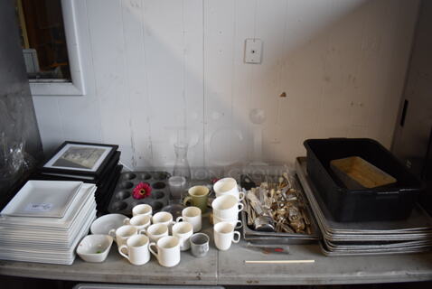 ALL ONE MONEY! Lot of Items on Tabletop Including Ceramic Plates, Ceramic Mugs, Silverware, Metal Baking Pans and Picture Frames.