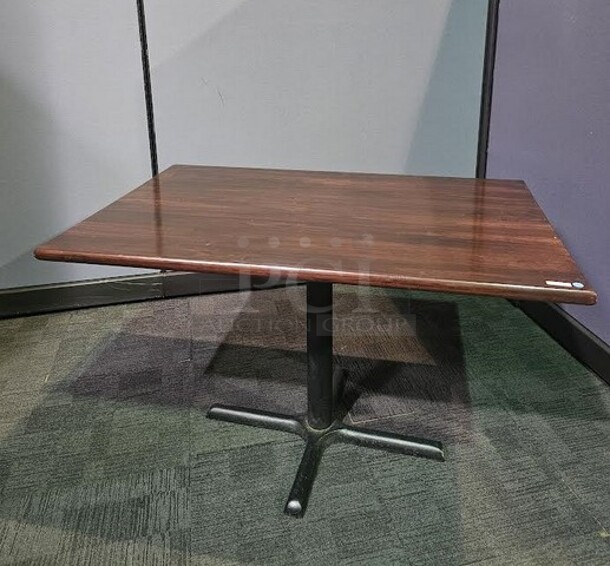 Restaurant style table with a black metal base and a dark grained wooden top. A solid table in good condition! Some scratching on base that can be cleaned up. 29” H x 48” W x 29.5” D.  

  - Image 2 of 2