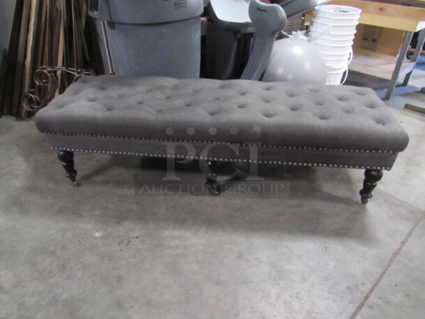 One Gray Cushioned Bench Seat With Nail Head Trim And Wooden Legs On Casters.  60X20X18