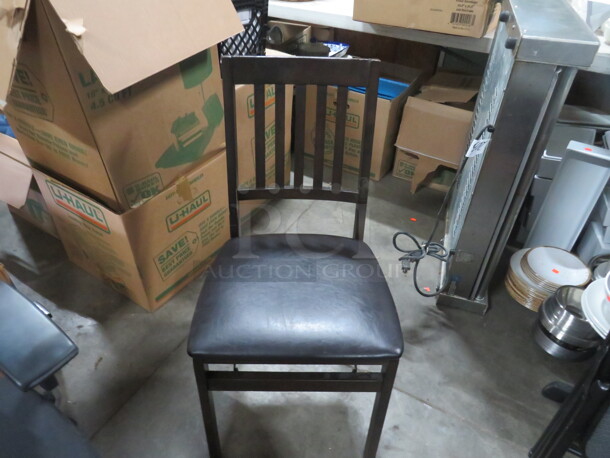One Wooden Folding Chair With Black Cushioned Seat.