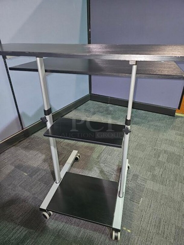 Adjustable-height mobile workstation with silver metal framing and black wooden surfaces. This workstation is on wheels and can be easily moved. In great used condition! Measures 44” H x 39.5” W x 33” D.  

 - Image 3 of 3