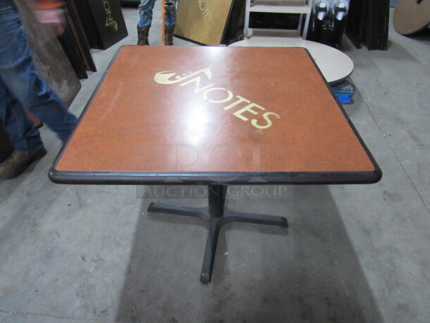 One Brown Table Top With The NOTES Logo On A Pedestal Base. 36X36X30
