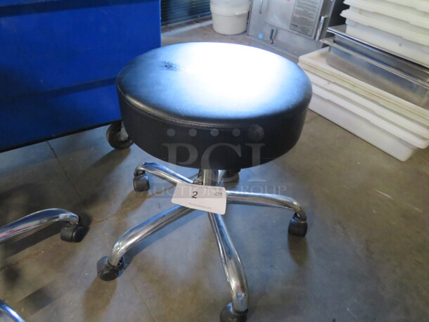 One Adjustable Height  Stool With Chrome Legs On Casters Wit A Black Cushioned Seat.